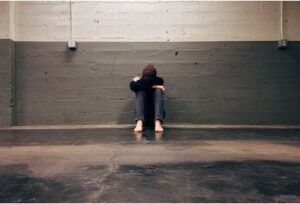 In un ambiente sguarnito un adolescente seduto in terra, con la schiena contro la parete, le braccia poggiate sulle gambe rannicchiate e la testa sulle braccia (foto su Pexels).