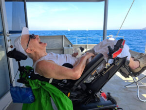 Un signore con SLA ride felice a bordo di una delle imbarcazioni coinvolte nella veleggiata organizzata dall’Associazione AISLA Piombino per la Giornata Mondiale della lotta alla SLA 2023.