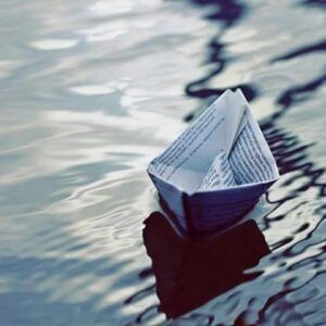 Una barchetta di carta naviga su uno specchio d’acqua increspata.