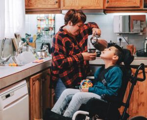 In una cucina una caregiver versa una bevanda ad un adolescente in sedia a rotelle (fonte: Fondazione Arezzo Comunità).