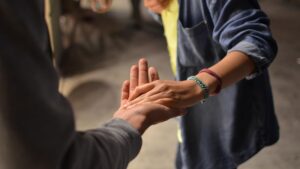 La mano di un caregiver incontra e sorregge quella di una persona con disabilità.