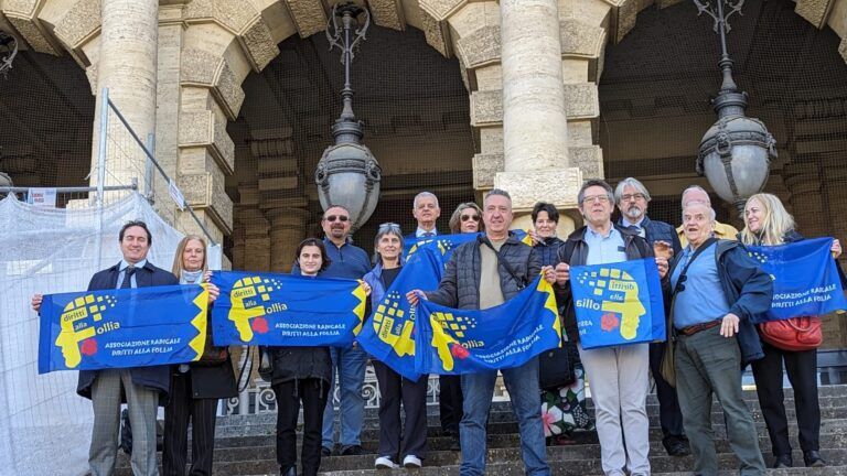 La delegazione dell’Associazione Diritti alla Follia mostra le bandiere dell’Associazione stessa sui gradini del palazzo della Corte Suprema di Cassazione, presso la cui Cancelleria ha depositato una Proposta di Legge per l’abolizione dell’interdizione, dell’inabilitazione, e per la riforma dell’amministrazione di sostegno (Roma, 18 aprile 2024).