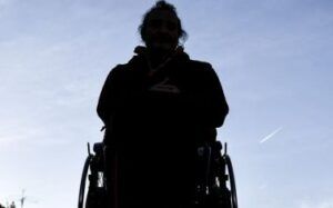 Una persona con disabilità ritratta in controluce con un cielo terso alle spalle.