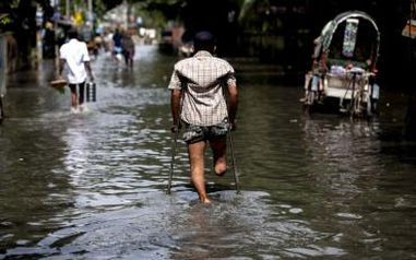 Un uomo con una gamba amputata si sposta con le stampelle in mezzo all’acqua in un luogo alluvionato.