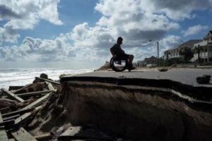 Una persona con disabilità in carrozzina lungo una parte di un’autostrada distrutta dall’Uragano Matthew a Flagler Beach, in Florida, il 9 ottobre 2016 (© Jewel Samad/AFP/Getty Images). Le persone con disabilità sono ancora sempre tra le più vulnerabili, in caso di emergenze climatiche.