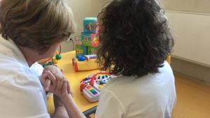 Una giovane con autismo, ritratta di spalle, esegue degli esercizi con dei giochi con l’aiuto di un’operatrice.