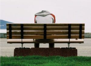 Una persona ritratta di spalle, seduta su una panchina, col capo chino (foto di Serkan Göktay su Pexels).