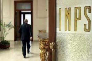 Un uomo in completo nero e ritratto di spalle si muove all’interno di un edifico. Sulla destra si vede il particolare di una posta con un vetro smerigliato su cui si legge la scritta INPS.