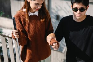Un giovane cieco sale una rampa di scale appoggiandosi al braccio di una giovane caregiver (foto di Eren Li su Pexels).