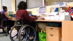 In un ufficio due persone lavorano al computer, una di esse è in sedia a rotelle.