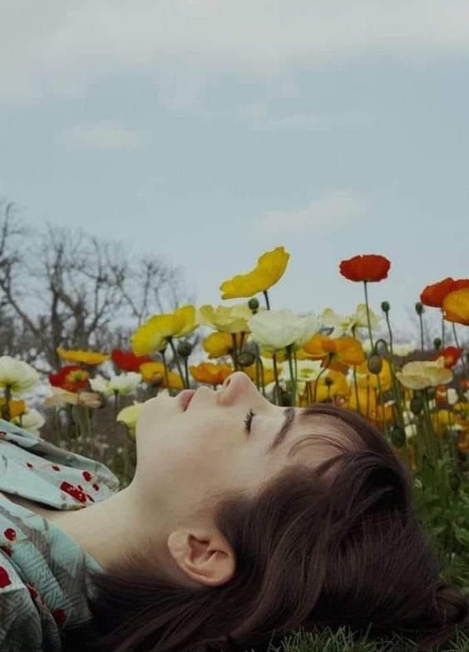 Particolare del viso di una giovane donna sdraiata su un campo di papaveri rossi, gialli e bianchi.