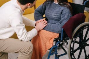 Particolare di un caregiver che tiene le mani di una donna in sedia a rotelle (foto di Ivan Samkov su Pexels).