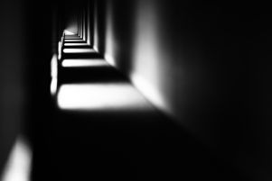 Makoto Sasaki, “La divisione del buio”. Fotografia in bianco e nero di un corridoio buio intervallato dalla porzioni di luce che scaturiscono da alcune aperture laterali.