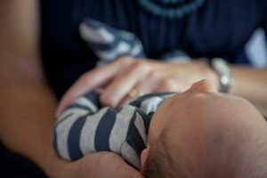 Particolare di una donna che tiene in grembo un neonato (foto di Tracey Shaw su Pexels).