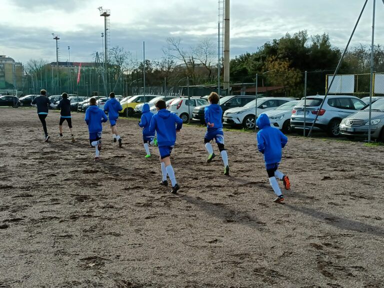 Alcuni degli atleti coinvolti nell’evento “Sport, Movimento ed Inclusione”, ritratti di spalle, mentre corrono in un campo sportivo sterrato.