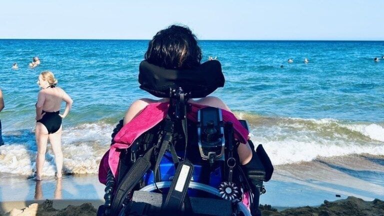 L’immagine scelta per illustrare la petizione lanciata da Paola Tricomi per l’autonomia e l’autodeterminazione di chi ha una disabilità motoria grave ritrae una persona con disabilità in sedia a rotelle, ritratta di spalle, mentre guarda il mare.
