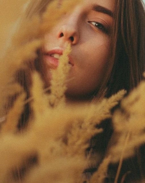 Un volto femminile parzialmente coperto da dei fiori color senape (foto di Dmitriy Zub su Pexels).